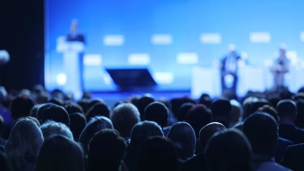 Business conference speaker presenting on stage to a large audience
